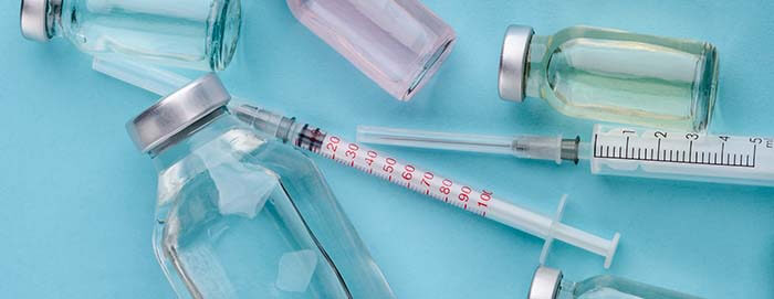 petites fioles de vaccins avec deux seringues sur fond bleu